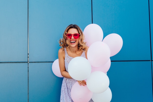 Free Photo young cute woman holding a bunch of air balloons, wearing pink sunglasses