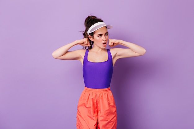 Young dark-haired woman in sports top and bright pants demonstrates strong hands