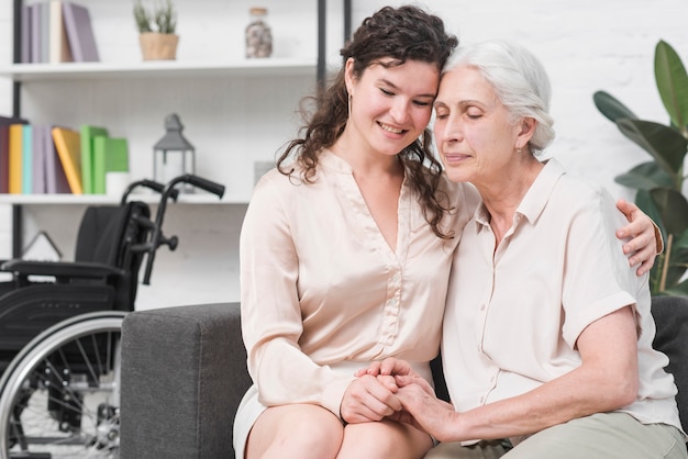 Young daughter sitting on sofa embracing her mother