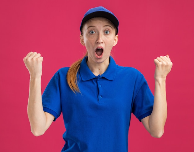 Free Photo young delivery girl in blue uniform and cap   amazed and surprised clenching fists