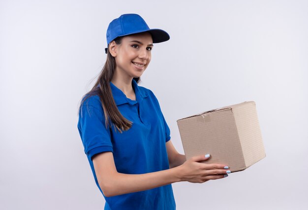 Young delivery girl in blue uniform and cap holding box package smiling confident 