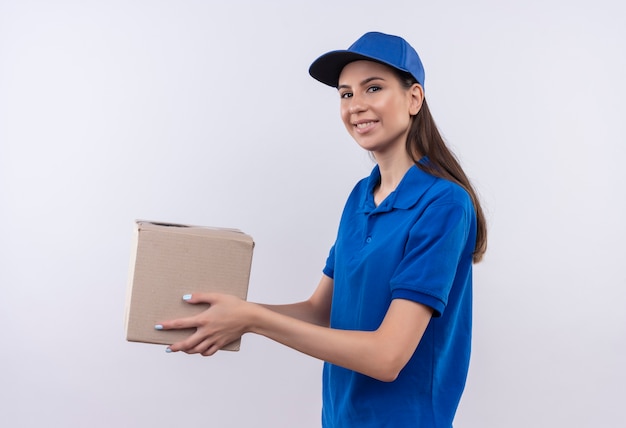 Young delivery girl in blue uniform and cap holding box package smiling confident 