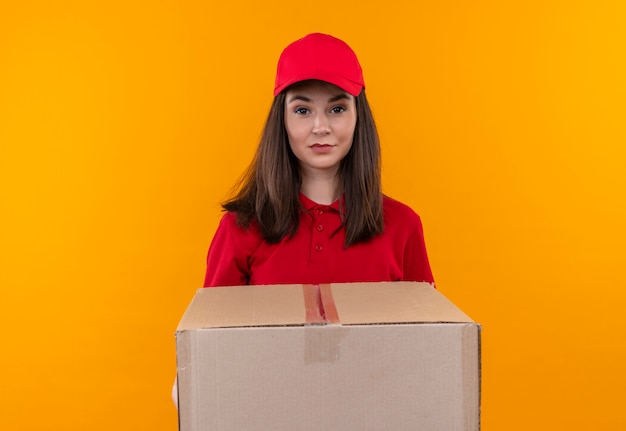 Young delivery girl wearing red t-shirt in red cap holding a big box on isolated yellow background