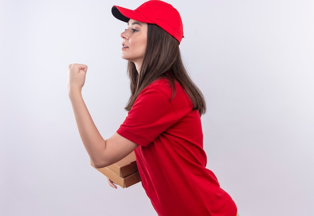 Young delivery girl wearing red t-shirt in red cap holding a pizza box and showing fist on isolated white background