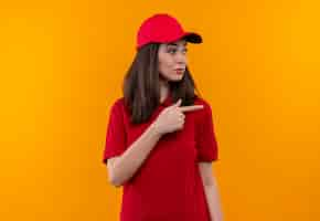 Free photo young delivery girl wearing red t-shirt in red cap points a finger to the side on isolated yellow background