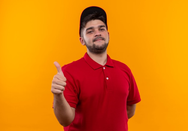 Young delivery man in red uniform and cap smiling showing thumbs up