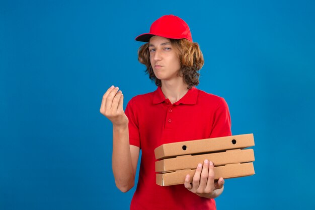 Young delivery man in red uniform holding pizza boxes making delicious gesture with hand smiling over isolated blue background