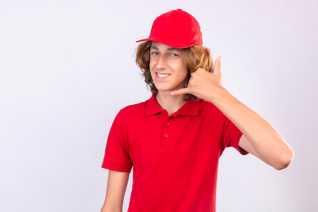 Young delivery man in red uniform making call me gesture looking confident smiling cheerfully over isolated white background