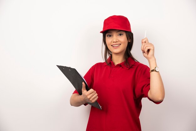 Young delivery woman in red uniform with clipboard on white background.