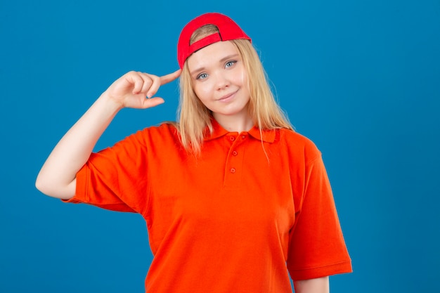 Free photo young delivery woman wearing orange polo shirt and red cap pointing temple with finger thinking focused on a task over isolated blue background