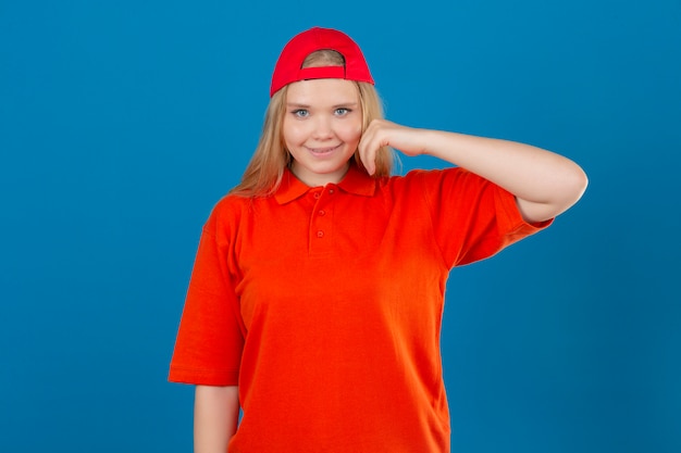 Free photo young delivery woman wearing orange polo shirt and red cap smiling happily touching cheek over isolated blue background