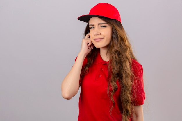 Free photo young delivery woman wearing red polo shirt and cap looking at camera squinting looking at camera with suspicion over isolated white background