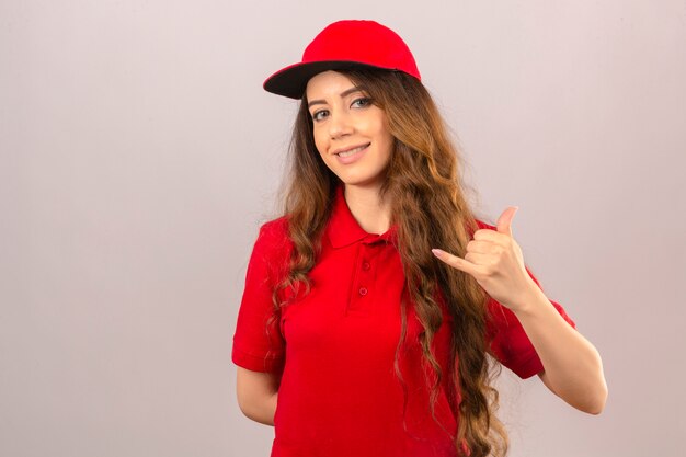 Young delivery woman wearing red polo shirt and cap making call me gesture looking confident over isolated white background