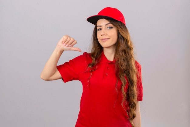 Free photo young delivery woman wearing red polo shirt and cap pointing thumb on herself smiling friendly over isolated white background