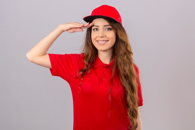 Free photo young delivery woman wearing red polo shirt and cap saluting looking at camera smiling friendly over isolated white background