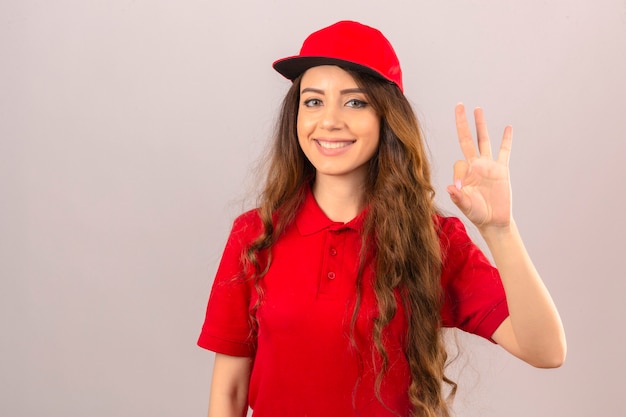 Free photo young delivery woman wearing red polo shirt and cap smiling friendly doing ok sign over isolated white background