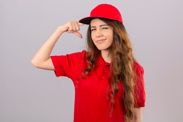 Free photo young delivery woman wearing red polo shirt and cap winking pointing temple with finger over isolated white background