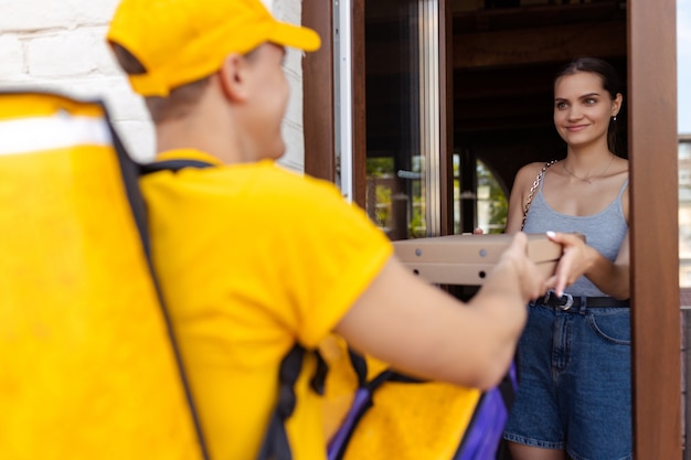 Young deliveryman in yellow uniform delivers order to clients idea of convenience speed comfort