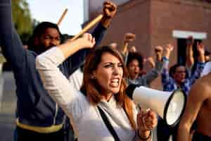 Free photo young displeased woman using megaphone and shouting while protesting with group of people on city streets