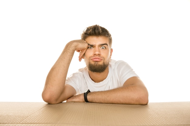 Free photo young dissapointed man opening the biggest postal package isolated on white. shocked male model on top of cardboard box looking inside.