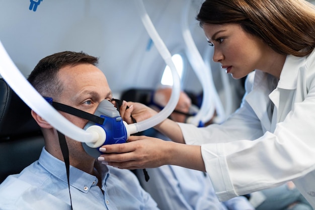 Young doctor assisting patient with a mask during hyperbaric oxygen therapy at clinic