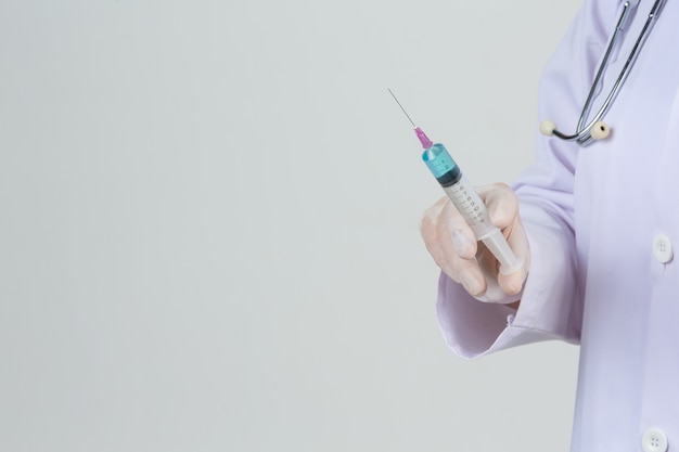 Young doctor is  holding  hypodermic syringe with  vaccine vial  rubber gloves on gray wall.