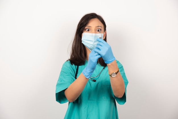 Young doctor with medical mask preparing syringe for injection on white background. High quality photo