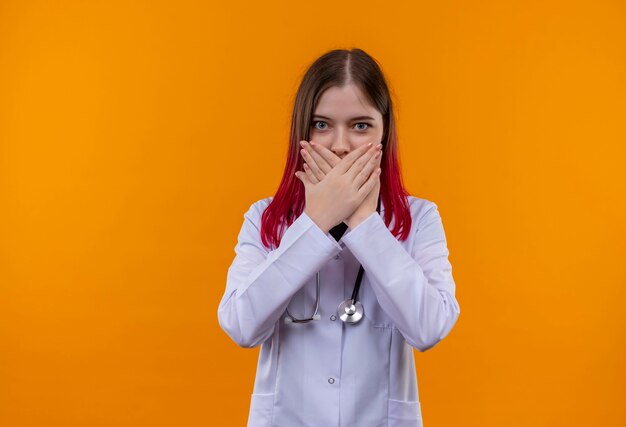  young doctor woman wearing stethoscope medical robe covered mouth with hands on isolated orange wall