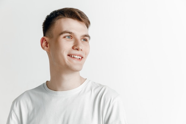 Young dreaming smiling man is waiting for chanses isolated on gray background. Dreamer at studio in white T-shirt