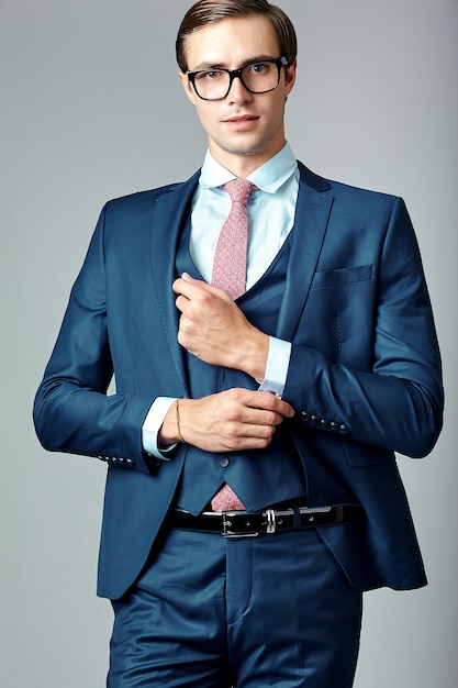 Young elegant handsome businessman male model in blue suit and fashionable glasses, posing in studio