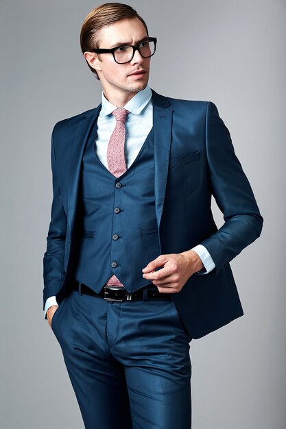 Young elegant handsome businessman male model in blue suit and fashionable glasses, posing in studio