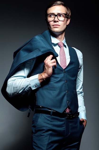 Young elegant handsome businessman male model in blue suit and fashionable glasses, posing in studio