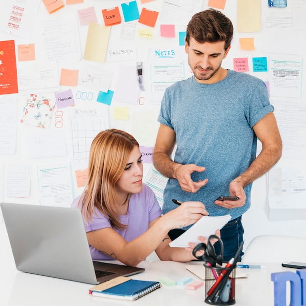 Free Photo young employees analyzing writings on notebook near workplace