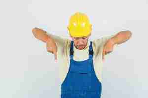 Free photo young engineer pointing down in uniform and looking focused. front view.