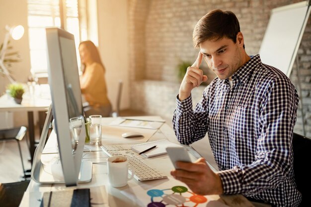 Young entrepreneur reading message on smart phone while working in the office