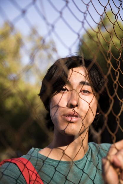 Young ethnic male looking at camera through wire fence