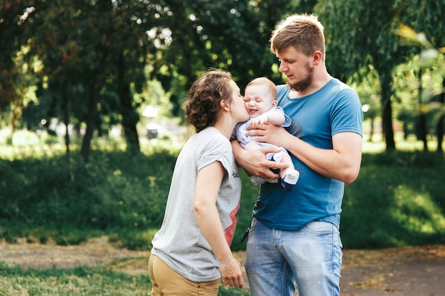 Young family, mother father and baby son happy posing in park