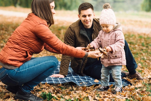 Young family playing with leaves in autumn forest