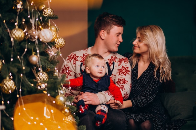 Young family with baby girl sitting by Christmas tree