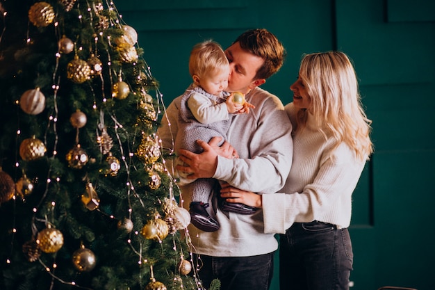 Young family with little daughter hanging toys on Christmas tree