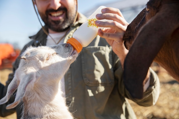 Free photo young farmer feeding his goats milk from a bottle at the farm