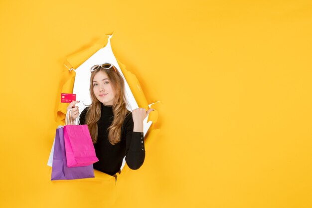 Young fashion woman holding shopping bags and credit card through torn paper hole in the wall