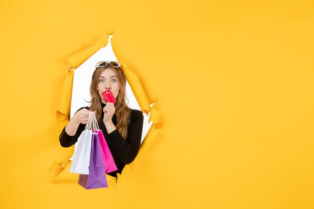 Young fashion woman holding shopping bags and credit card through torn paper hole in the wall