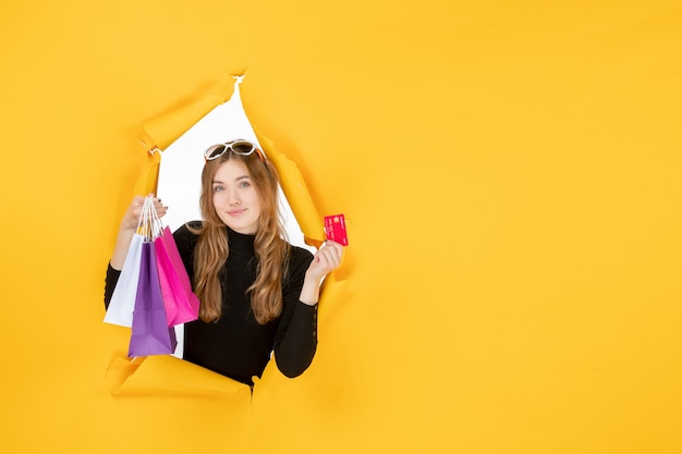 Young fashion woman holding shopping bags and credit card through torn paper hole in the wall