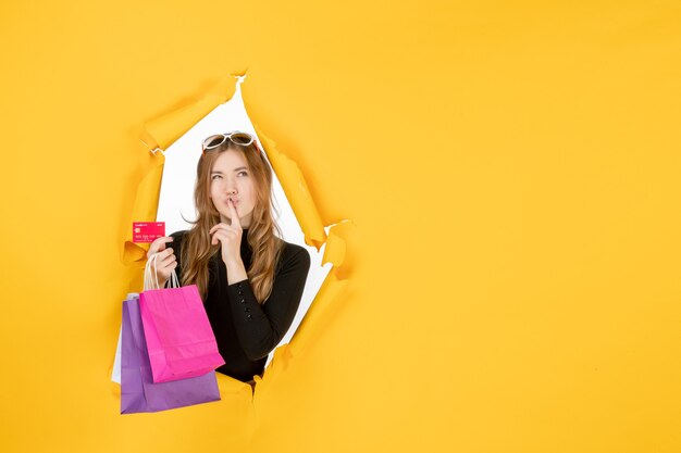 Young fashion woman holding shopping bags and credit card through torn paper hole in the wall