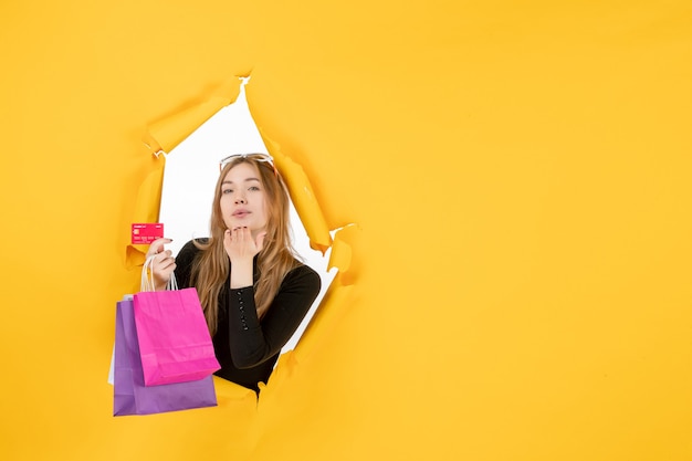 Young fashion woman holding shopping bags and credit card through torn paper hole in the wall