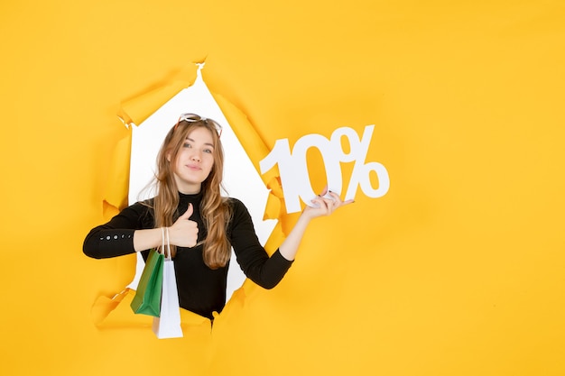 Young fashion woman holding shopping bags and discount percentage through torn paper hole in the wall