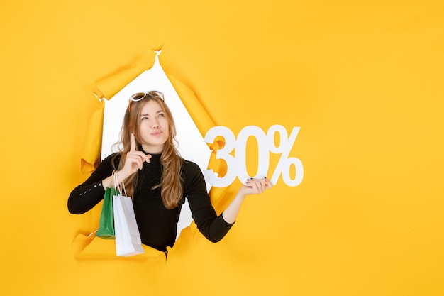 Young fashion woman holding shopping bags and discount percentage through torn paper hole in the wall