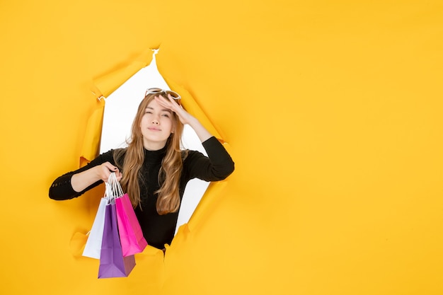 Free Photo young fashion woman with shopping bags through torn paper hole in the wall