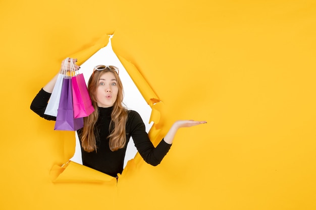 Young fashion woman with shopping bags through torn paper hole in the wall